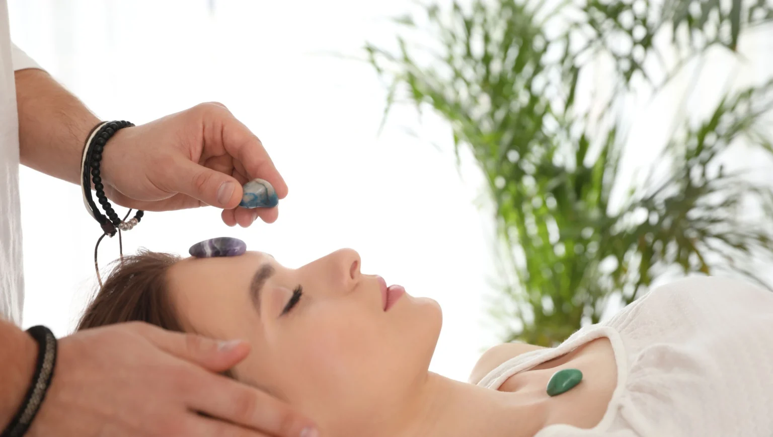 A practitioner using different energy healing tools such as crystals, sound bowls, and light touch in a peaceful setting
